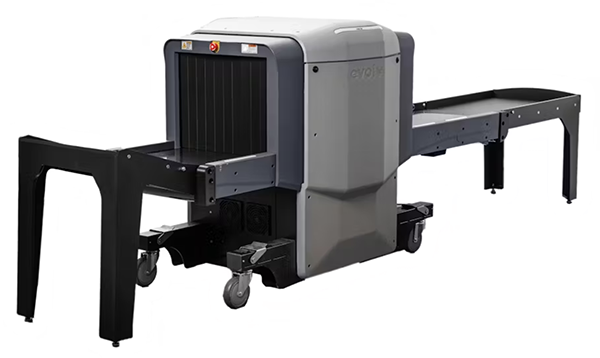 An airport security X-ray baggage scanner with a conveyor belt. The machine is gray and black, featuring a central scanning unit with wheels for mobility. The design is typical for scanning luggage at security checkpoints.
